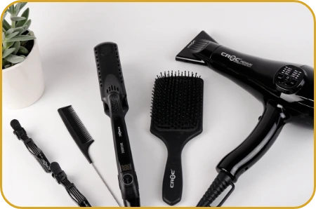 A collection of hair styling tools, including a black hair dryer, a comb, a brush, and a hairbrush